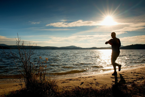 Mies urheilija tarkkailun aikana harjoitus run käyttää ulkona valtameren rannalla aurinkoinen kylmä aamu
 - Valokuva, kuva