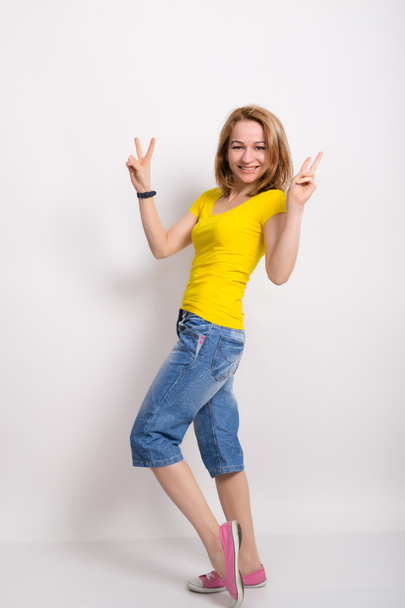 beautiful blonde girl in the yellow shirt, blue breeches shows gesture Victoria - Фото, изображение