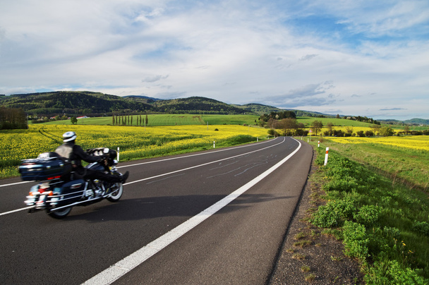 Motorcycle traveling along an empty asphalt road between yellow blooming rape fields - Photo, Image