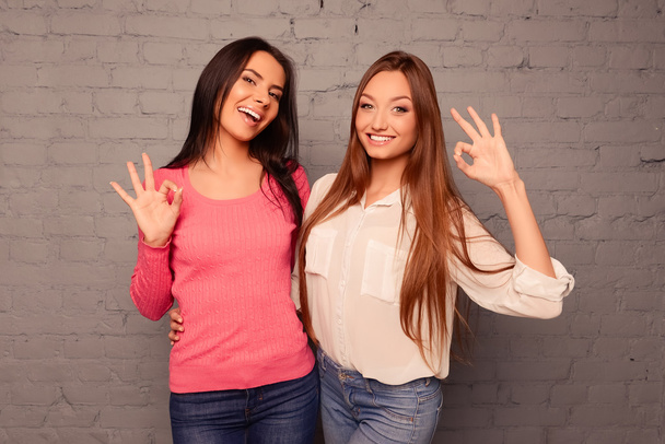 Happy girls gesturing ok with fingers and hugging - Фото, изображение