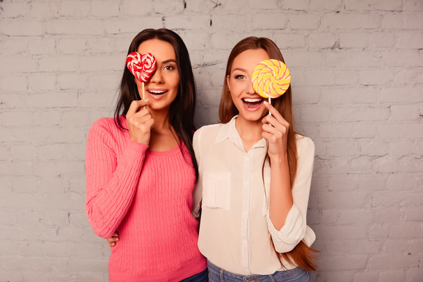  Two happy  girls rejoicing with  lollipop and smiling - Foto, imagen