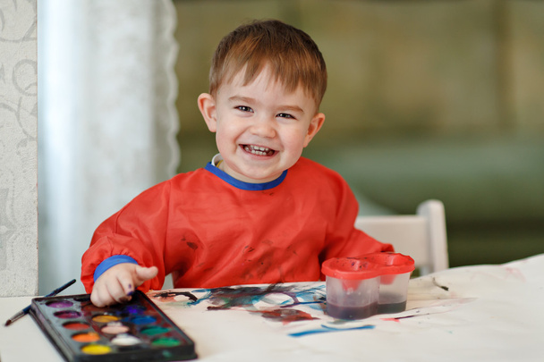 Small charming baby boy in a red robe draws colored paint sittin - Foto, immagini