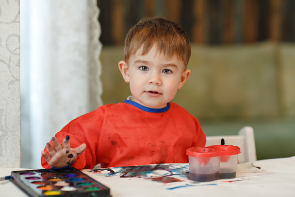 Small charming baby boy in a red robe draws colored paint sittin - Foto, Imagen