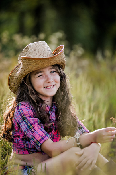 meisje zittend in een veld met een cowboy hoed - Foto, afbeelding