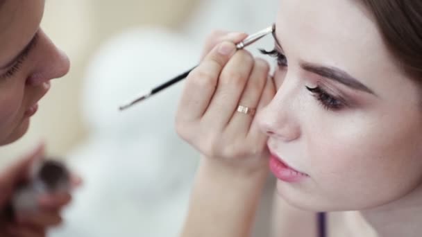 Makeup artist corrects the eyebrow line of model with the brush - Filmati, video