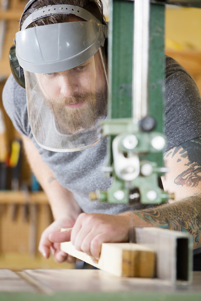 Handwerker mit Schutzmaske greift in Werkstatt zur Bandsäge - Foto, Bild