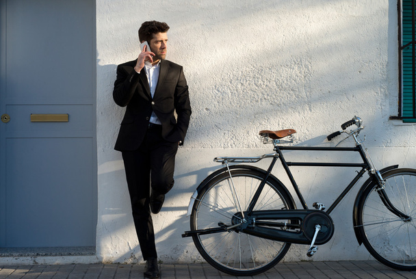 бизнесмен с велосипедом слушает телефон, поддерживаемый в
 - Фото, изображение