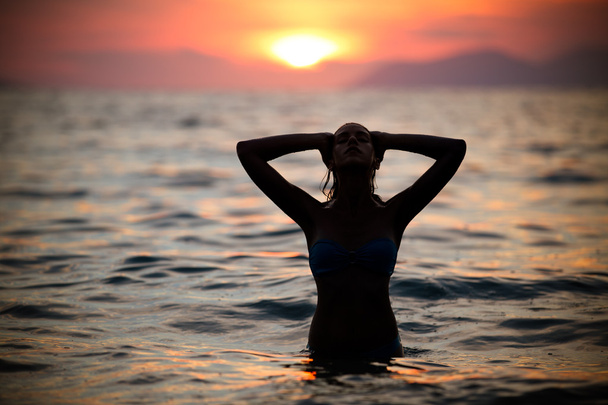 ゴージャスなセクシーなフィット女性シルエット水泳日没。無料幸せな女楽しむサンセット。夕日の黄金の太陽の光輝きを受け入れ、平和、自然の静けさを楽しむ水で美しい女性. - 写真・画像
