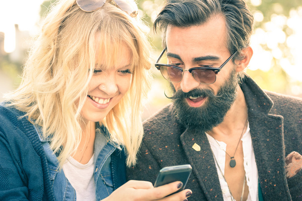 Ευτυχισμένο νεαρό ζευγάρι με vintage ρούχα που διασκεδάζουν με το smartphone-έναρξη της ιστορίας της αγάπης με χίππις καλύτεροι φίλοι στο κινητό τηλέφωνο-έννοια εθισμός με νέα τεχνολογία-ρηχά βάθος του πεδίου - Φωτογραφία, εικόνα