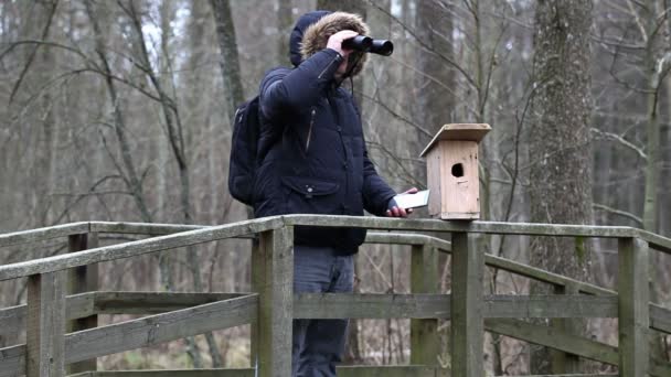 Ornitolog z lornetki i tablet Pc w pobliżu klatka dla ptaków - Materiał filmowy, wideo