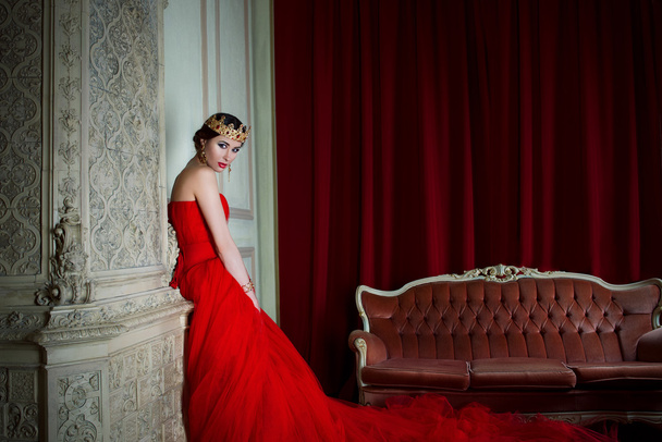 Όμορφο κορίτσι στο μάξι κόκκινο φόρεμα και στο βασιλικό στέμμα - Φωτογραφία, εικόνα