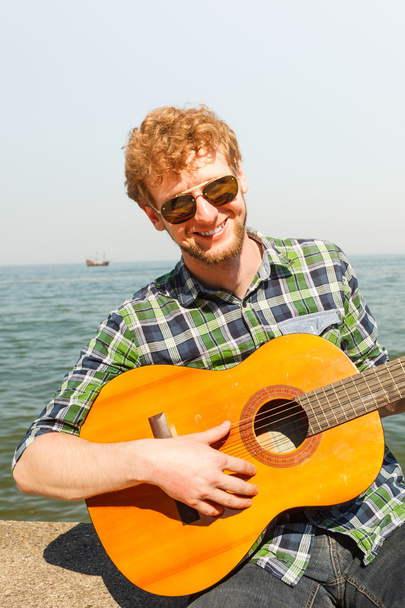 Young man hipster playing guitar by sea ocean. - Fotó, kép