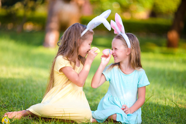 Két imádnivaló kicsi nővér játszó tojás visel nyuszi füle, húsvét napján - Fotó, kép