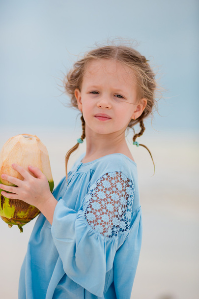 kleines entzückendes Mädchen trinkt Kokosmilch am Strand - Foto, Bild