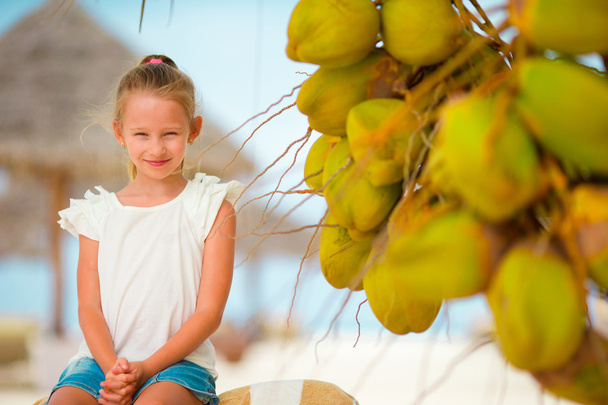 kleines entzückendes Mädchen mit Kokosnuss am weißen tropischen Strand - Foto, Bild