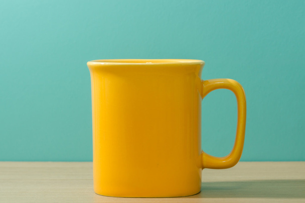 木製テーブルの上の黄色のマグカップ - 写真・画像