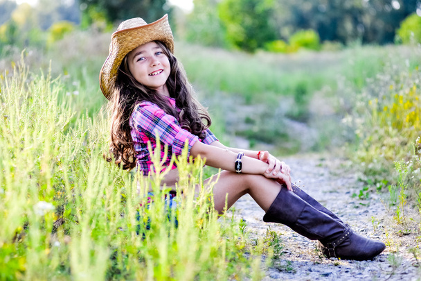 niña sentada en un campo con un sombrero de vaquero
 - Foto, Imagen