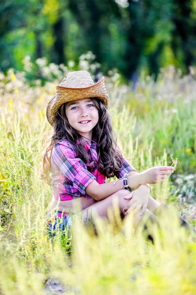 petite fille assise dans un champ portant un chapeau de cow-boy
 - Photo, image