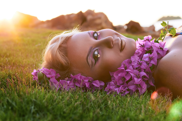 Mulher bonita deitada na grama, flores perto do rosto, maquiagem brilhante
 - Foto, Imagem
