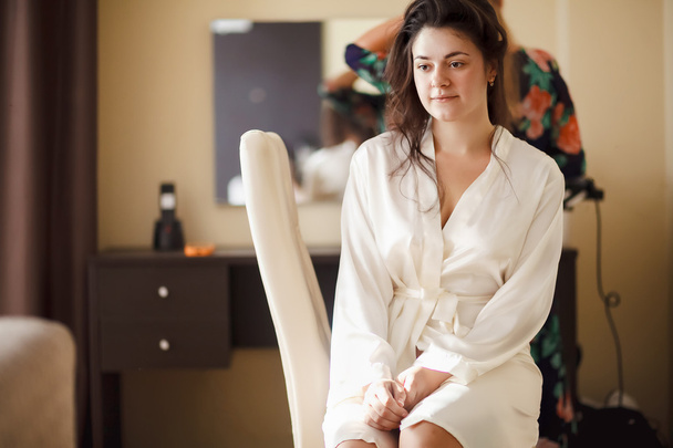 The bride in white bathrobe with her hair done at morning. Wedding preparations. - Foto, afbeelding
