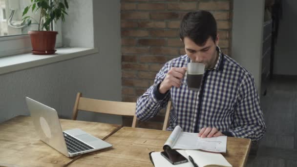 En el café, el hombre sentado en una mesa leyendo una revista y bebiendo café
. - Metraje, vídeo