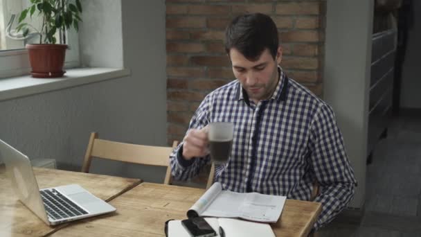 Hombre atractivo bebiendo café y leyendo el periódico, está en la mesa teléfono y un ordenador portátil
. - Metraje, vídeo