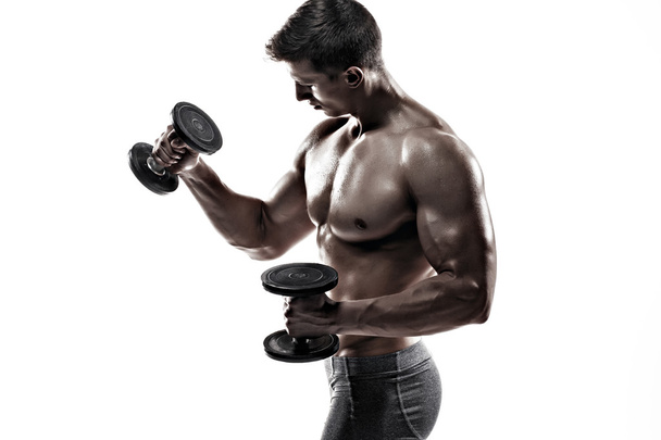 Athletic man showing muscular body and doing exercises with dumbbells - Foto, afbeelding