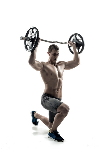 Muscular man standing on knee, holding barbell over his head - 写真・画像