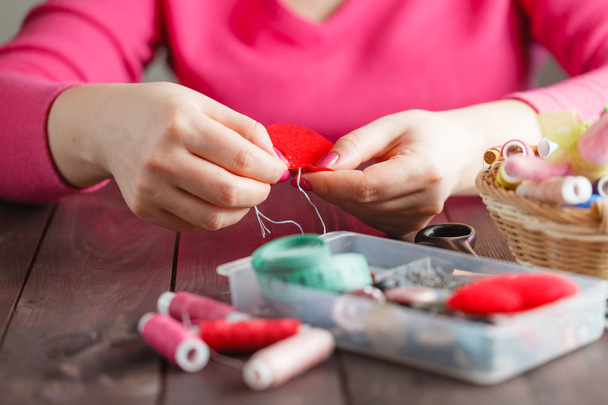 Woman sews red heart shaped toy by needle - Foto, afbeelding