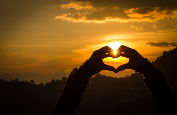 Силуети ручної форми серця з сонячними наборами і оранжевим небом
 - Фото, зображення