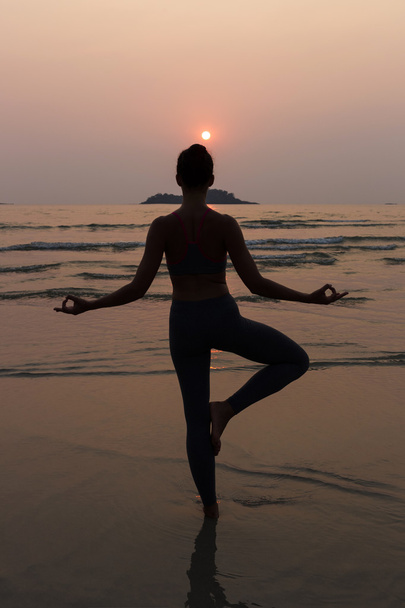 Młoda szczupła kobieta praktykujący stanowią od jogi na plaży o zachodzie słońca - Zdjęcie, obraz