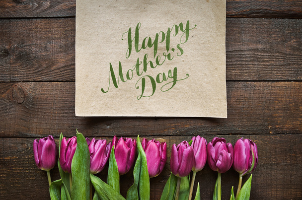 Hapy anya nap ecset nib betűkkel kalligráfia. Rózsaszín tulipán csokor pajta sötét fából készült deszka háttér. Levelezőlap-sablonok. - Fotó, kép
