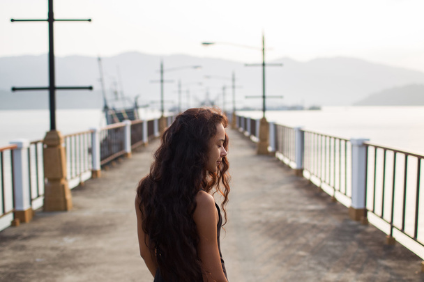 Женщина с длинными черными волосами ходит по пустому мосту утром
 - Фото, изображение