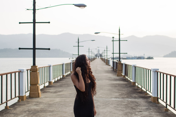 Frau in schwarzem Kleid beobachtet Sonnenaufgang an der leeren Brücke. Morgenstimmung - Foto, Bild