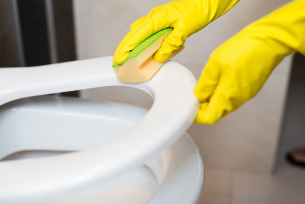  handen reinigen van de wc-bril in wc met gele spons - Foto, afbeelding