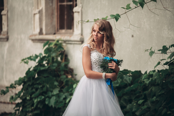 Luxury young blond bride with bridal bouquet poses on the background gorgeous plants - Фото, изображение