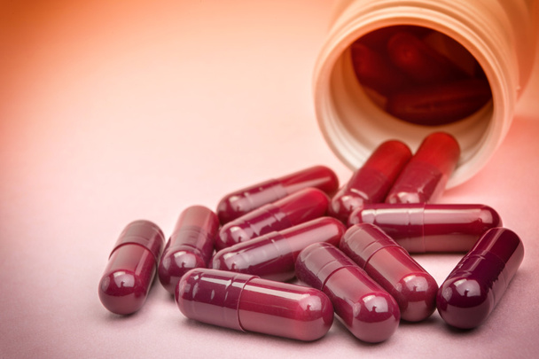 A rózsaszín háttér elszigetelt nyitott üveg ömlött tabletták - Fotó, kép