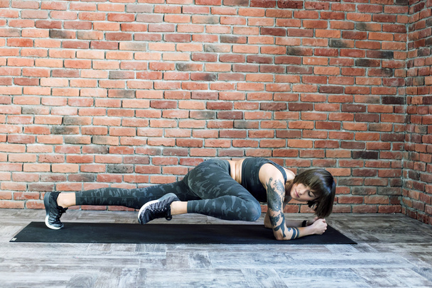 tattooed female doing exercises indoors, sporty woman practicing yoga - Fotó, kép