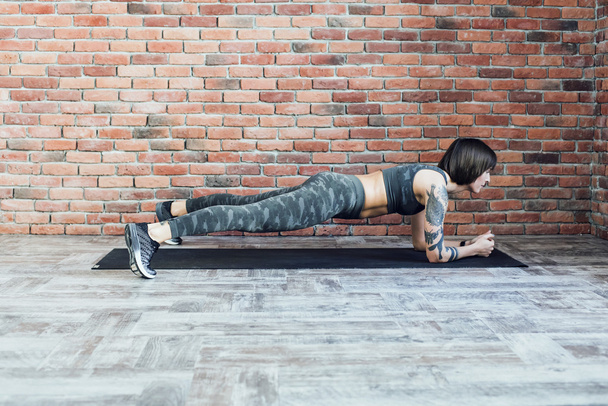 tattooed female doing exercises indoors, sporty woman practicing yoga - Valokuva, kuva