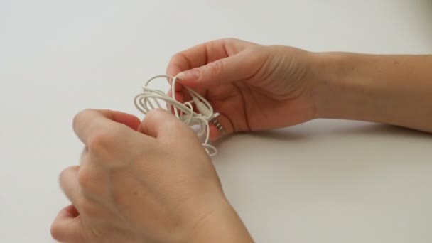 Woman untangles tangled earbuds or earphone knot - Footage, Video