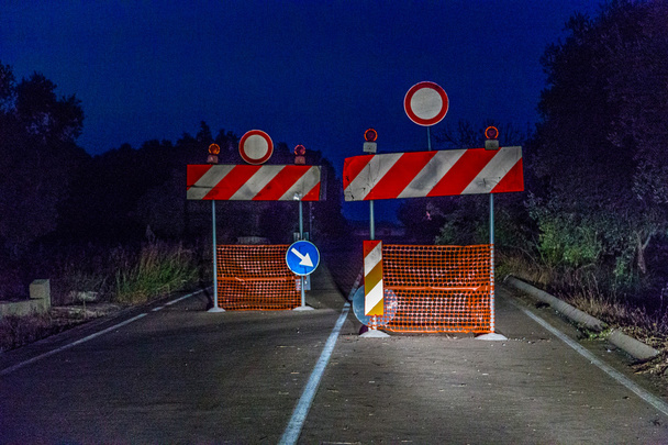 sinais que proíbem o acesso a uma estrada interrompida iluminada pelos faróis de um carro à noite
 - Foto, Imagem