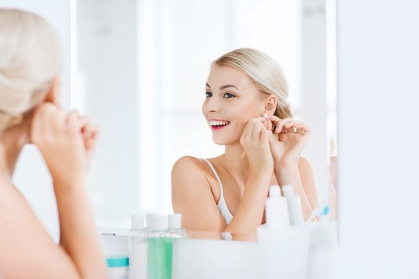 woman trying on earring looking at bathroom mirror - Fotó, kép