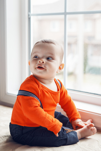 Portrait of cute adorable Caucasian baby boy sitting on windowsi - Photo, Image