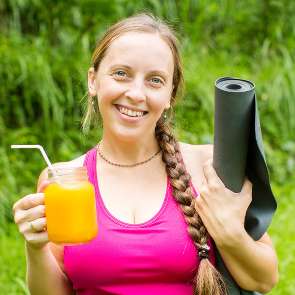 Fitness woman with yoga mat holding a glass of orange juice - Foto, Imagen