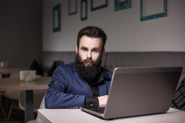 homme barbu en costume et avec ordinateur portable assis dans le café et la navigation
 - Photo, image