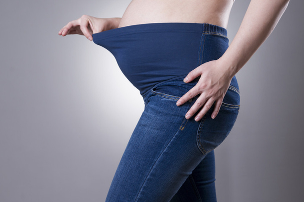 Pregnant woman in blue jeans for pregnant women on gray background - Fotografie, Obrázek