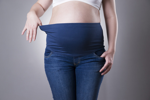 Вагітна жінка в блакитних джинсах для вагітних на сірому фоні
 - Фото, зображення