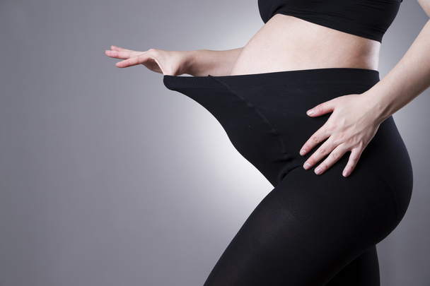 Pregnant woman in black tights for pregnant women on gray background - 写真・画像