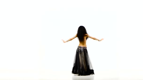 Beautiful young exotic belly dancer with long dark hair in unusual suit shaking her hips and bends, on white - Filmati, video