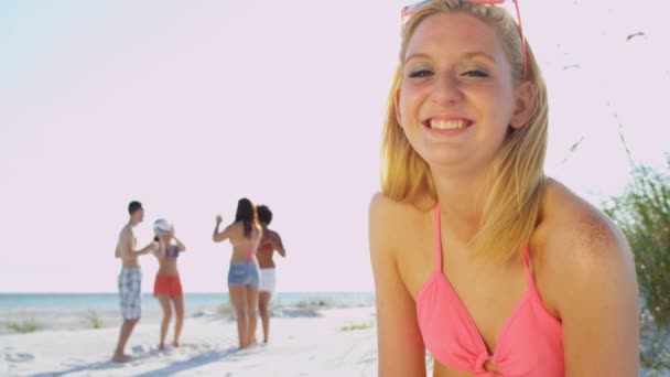 dziewczyna siedzi na plaży, a przyjaciele grać w piłkę - Materiał filmowy, wideo